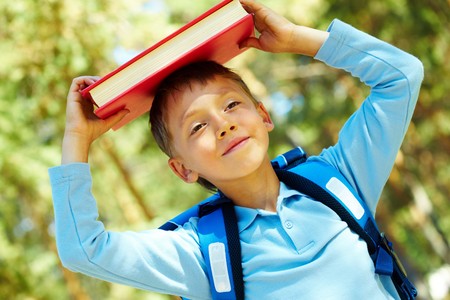 Photo of diligent schoolboy with book on his head outdoorの写真素材