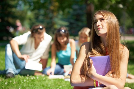 Portrait of teenage girl with book in hands on background of her reading friendsの写真素材