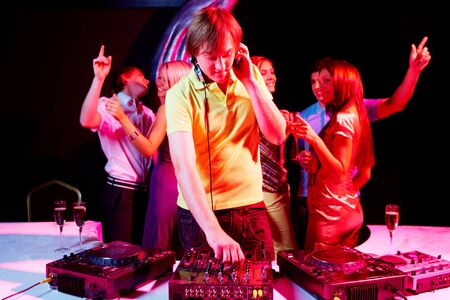 Portrait of handsome deejay working with dancing teens on background