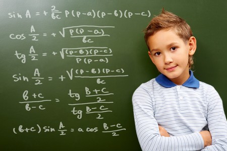 Portrait of smart schoolchild by the blackboard with sums on it looking at cameraの写真素材
