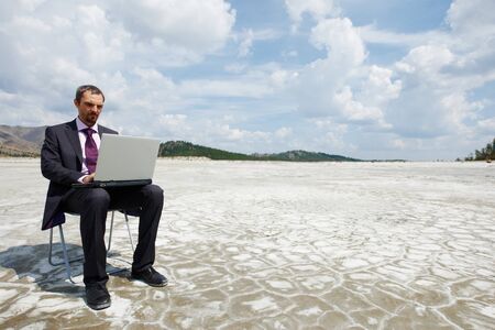 Photo of modern businessman typing on laptop outside with cloudy sky aboveの写真素材