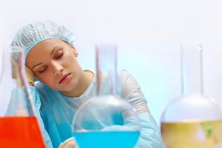 Tired nurse sleeping in laboratory with several flasks in frontの写真素材
