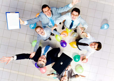 Above view of joyful business people looking at camera with balloons on the floor 