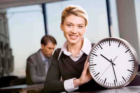 Portrait of representative woman sitting at the table and holding clock