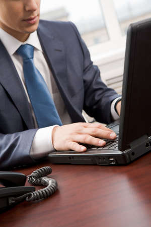 Close-up of businessmans hand pressing keys of laptop in officeの写真素材