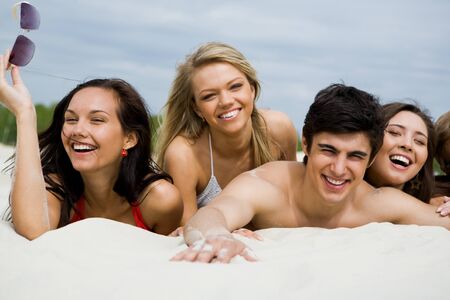 Photo of pretty girls and happy guy lying on sandy beach at leisureの写真素材