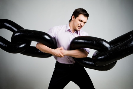 Portrait of tense businessman with two sections of huge chain over grey backgroundの写真素材