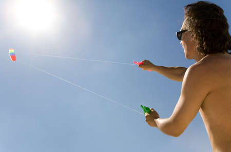 Image of young man flying a colorful kite into bright blue sky with shining sun upwardsの写真素材