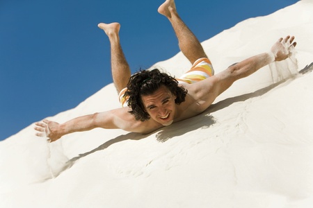 Happy guy lying on sand with outstretched arms and looking at camera on beachの写真素材