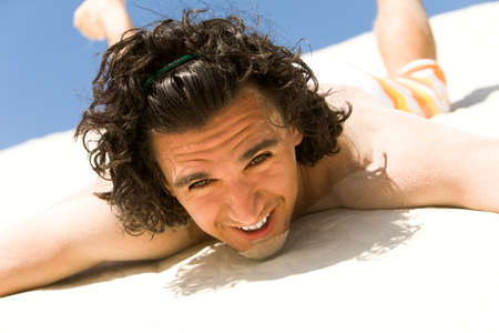 Happy guy lying on sand with outstretched arms and looking at camera on beachの写真素材