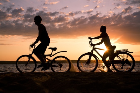 Silhouettes of couple riding their bicycles on seashore at sunsetの写真素材