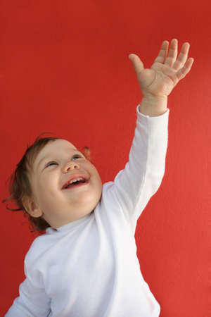 Portrait of happy toddler looking upwards and stretching her hand over red backgroundの写真素材
