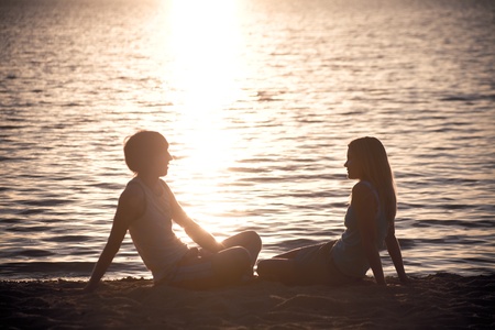 Photo of serene couple sitting on the seashore and talking at sunsetの写真素材