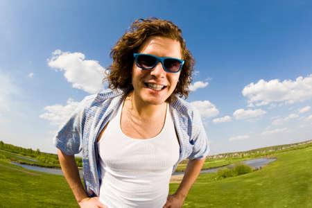 Portrait of young man in sunglasses looking at camera on background of countrysideの写真素材