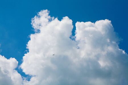Photo of bright cloudy sky with flying airplane in itの写真素材