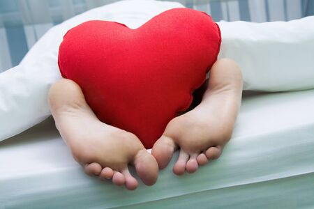 Image of bare feet with red soft heartshaped pillowの写真素材