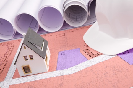 Close-up of toy house model on blueprints with helmet near by
