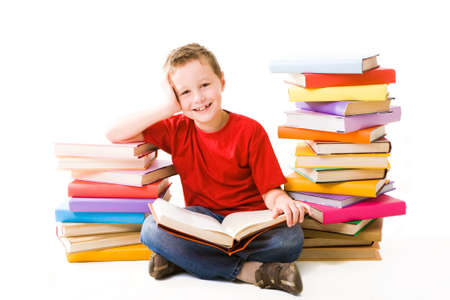 Image of schoolboy sitting between two heaps of books and reading one of them