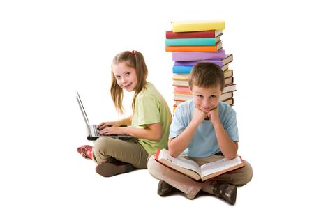 Smart girl with laptop and cute schoolboy with book sitting back to back and looking at cameraの写真素材