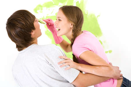 Image of joyful girl painting lads face with green color while both laughing during improvement of flatの写真素材