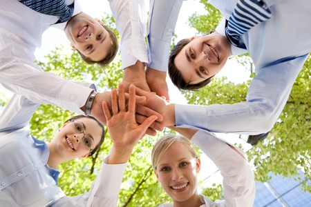 Bottom view of people making pile of hands on background of green foliage