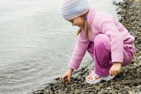 Pretty girl in violet clothes touching pebbles by the riverの写真素材