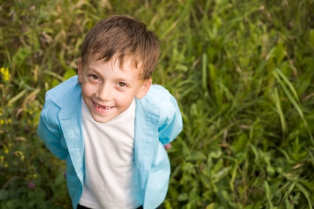 Above shot of happy boy standing on green grass and smiling at cameraの写真素材