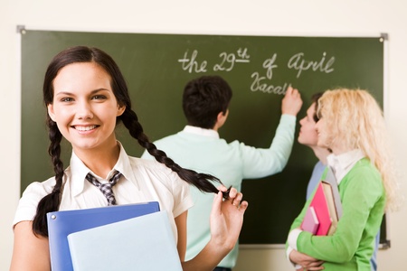 Portrait of cute girl holding textbook in hands on background of communicating studentsの写真素材