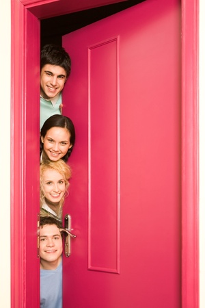 Portrait of happy students looking from behind door at camera with smilesの写真素材