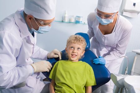 Image of cute boy talking to dentist and his assistant before mouth checkupの写真素材