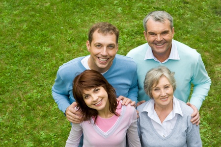 Above angle of senior and young couples standing on green grass and looking upwards at camera