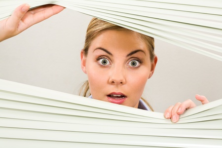 Portrait of surprised woman looking at camera out of venetian blindの写真素材