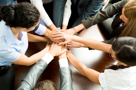 Above angle of business partners making pile of hands on workplace  