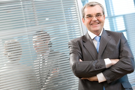 Image of senior leader smiling at camera on background of venetian blind