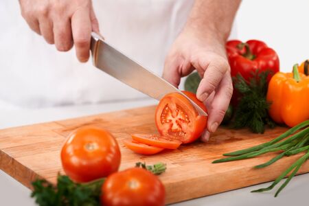 Image of male hand with knife cutting tomatoes on wooden chopping board