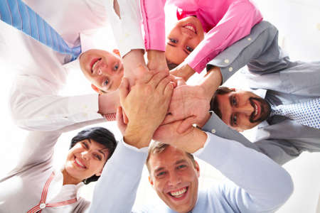 Below shot of smiling co-workers making pile of hands and looking at camera