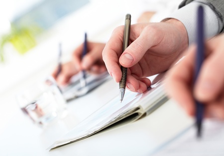 Row of human hands with pens making notes during conferenceの写真素材