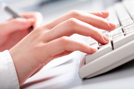 Close-up of female hands touching buttons of white keyboard and holding pen の写真素材