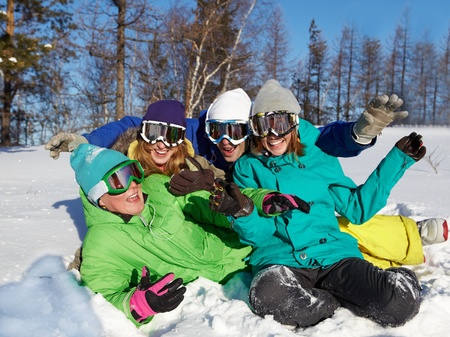 Portrait of four laughing teenagers in ski goggles sitting on snow