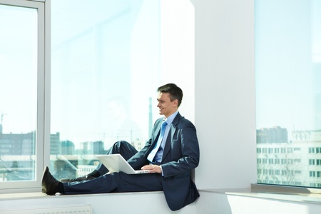 Portrait of confident man sitting with laptop in officeの写真素材