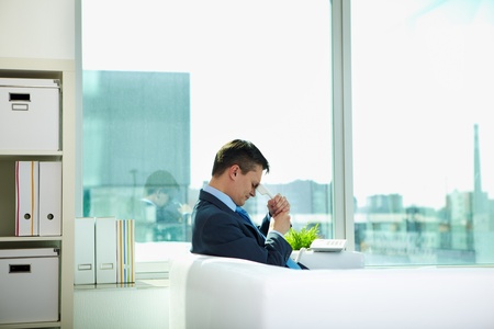 Sad businessman sitting on sofa with phone receiver in officeの写真素材