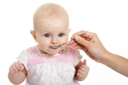 Adorable baby being fed from spoon by her mother handの写真素材