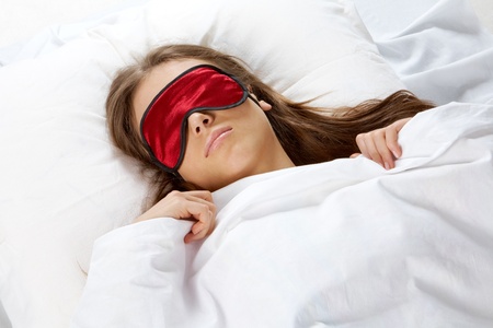 Portrait of a young girl with eye mask sleeping under blanketの写真素材