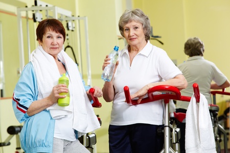Portrait of senior females with plastic bottles looking at camera in gymの写真素材
