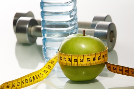 Closeup of green apple with measuring tape and two metal barbells on background の写真素材