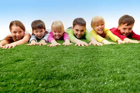 Group of happy children lying on a grass and stretching their arms の写真素材