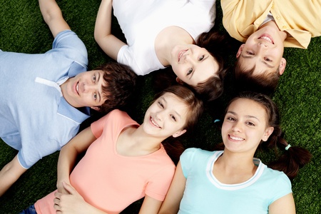 High angle view of five happy teens lying on grass の写真素材