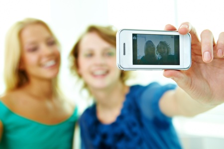 Happy girls taking photo of themselves on telephone cameraの写真素材