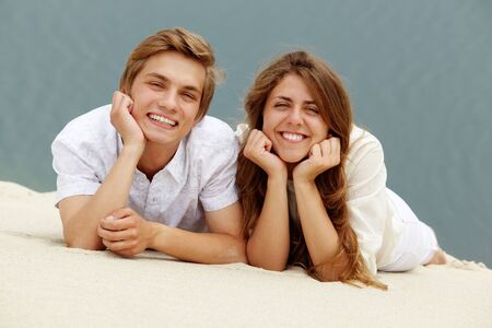 Photo of happy couple lying on sand and looking at camera の写真素材