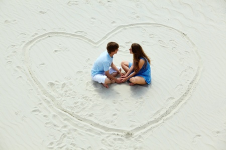 Photo of happy couple sitting on sand in the center of heart の写真素材